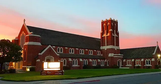 A picture of Compass Church Padre Dr. campus, Monterey County, with a tall tower, green lawn, and a colorful sunset.