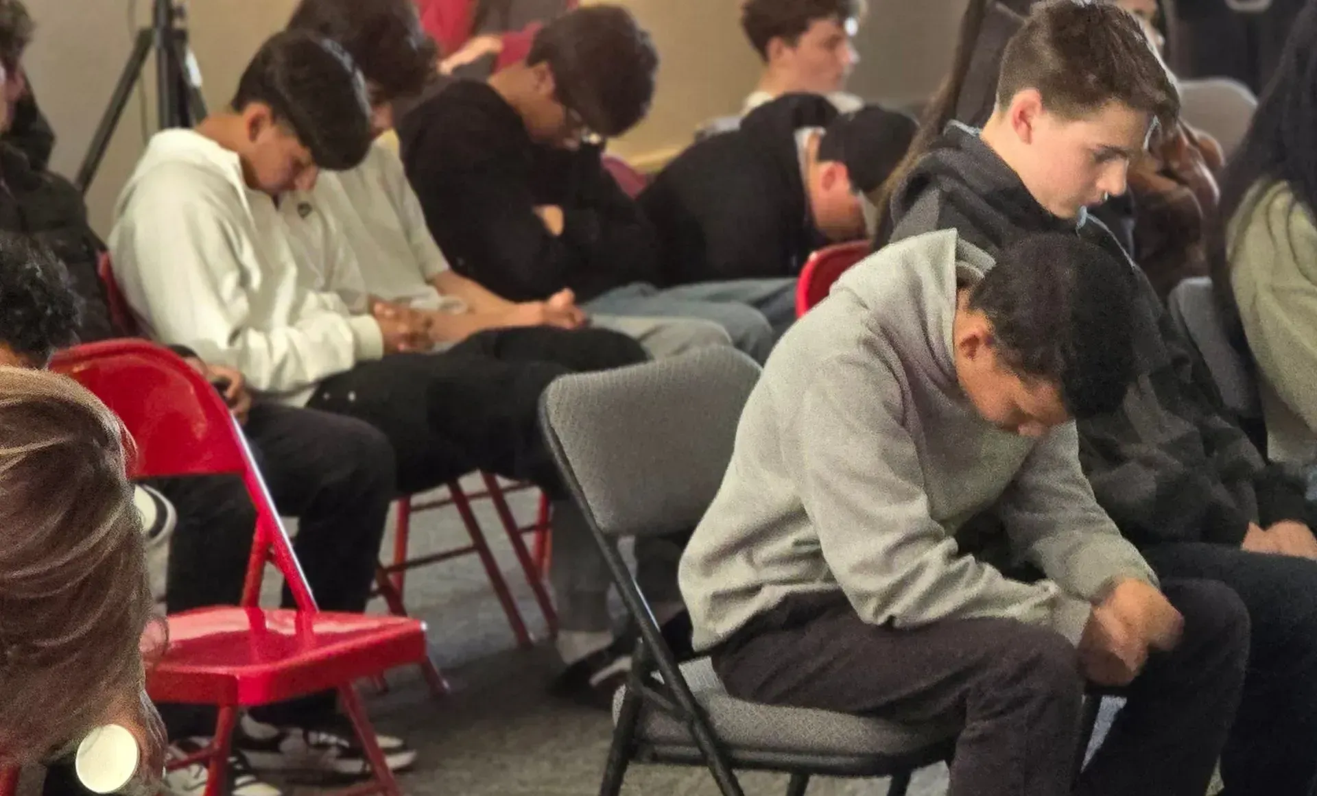 Group of people in a room, heads bowed, possibly praying or in silent reflection.