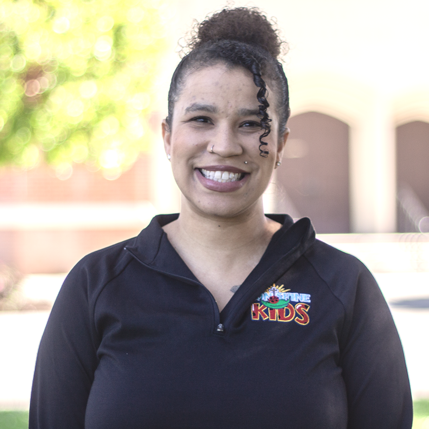 Woman with curly hair in a black top smiles outdoors, 