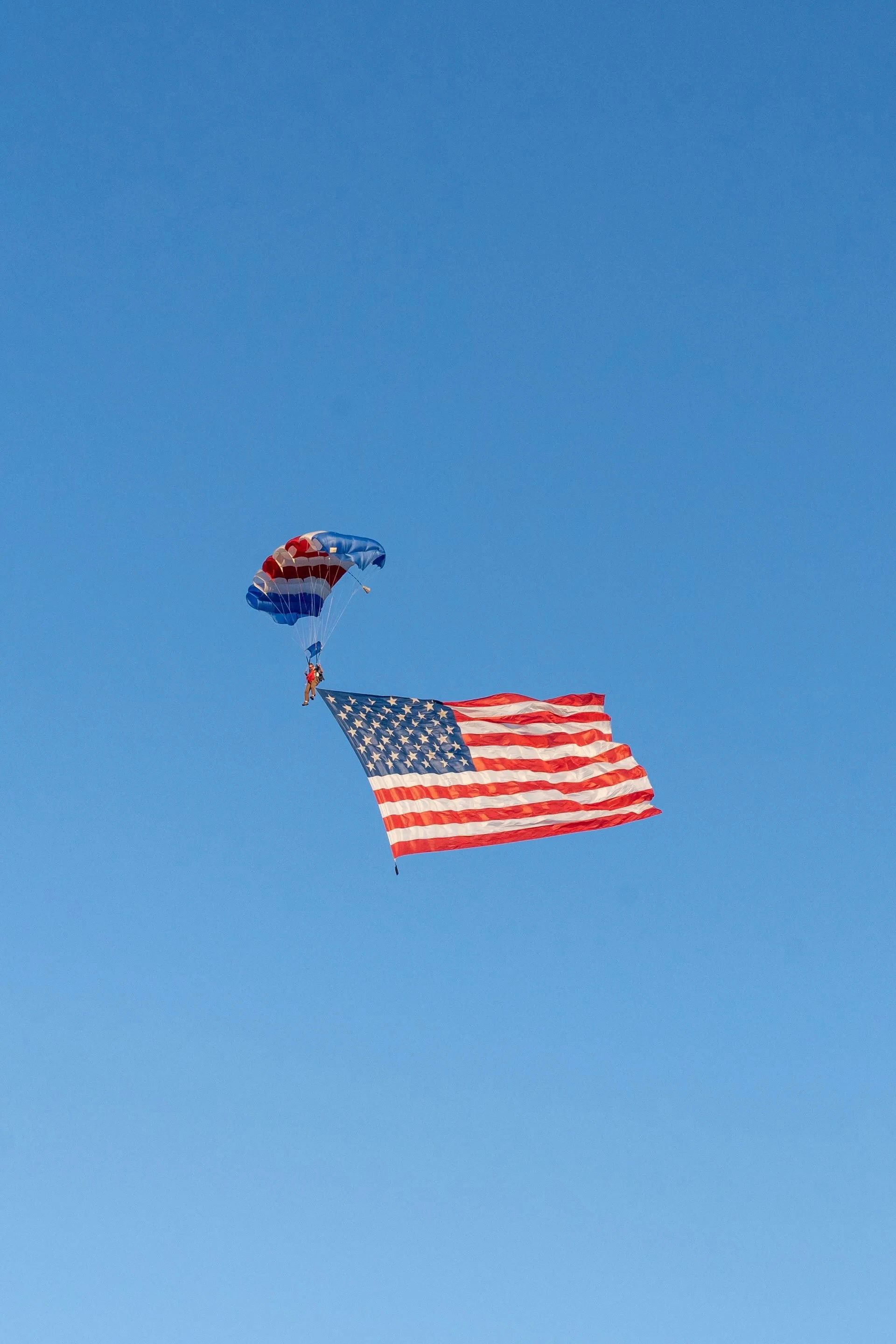 Skydiving with the American flag. A person under a parachute carrying the flag against a blue sky.