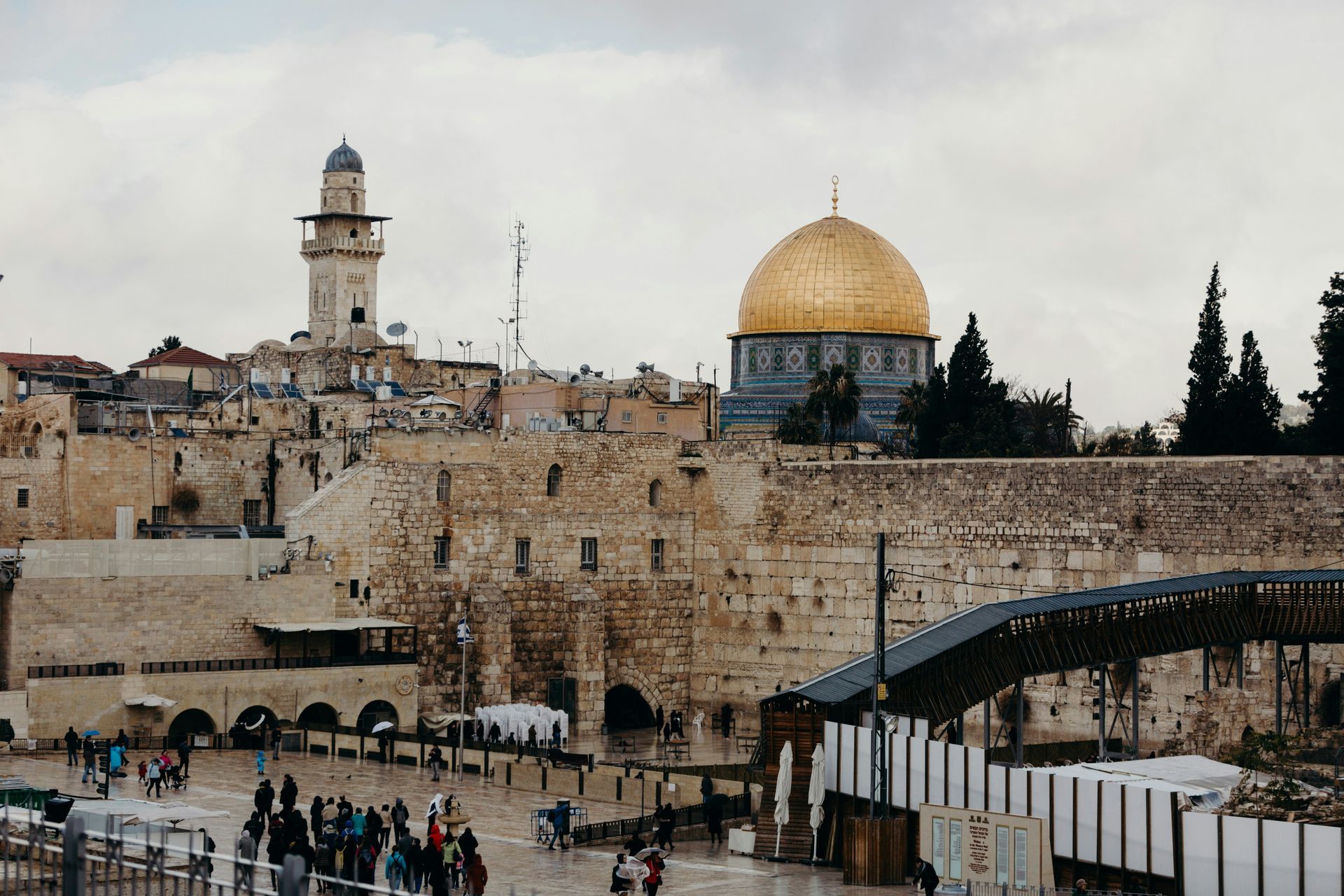 Jerusalem skyline: Western Wall, Dome of the Rock with gold dome, minaret, people.