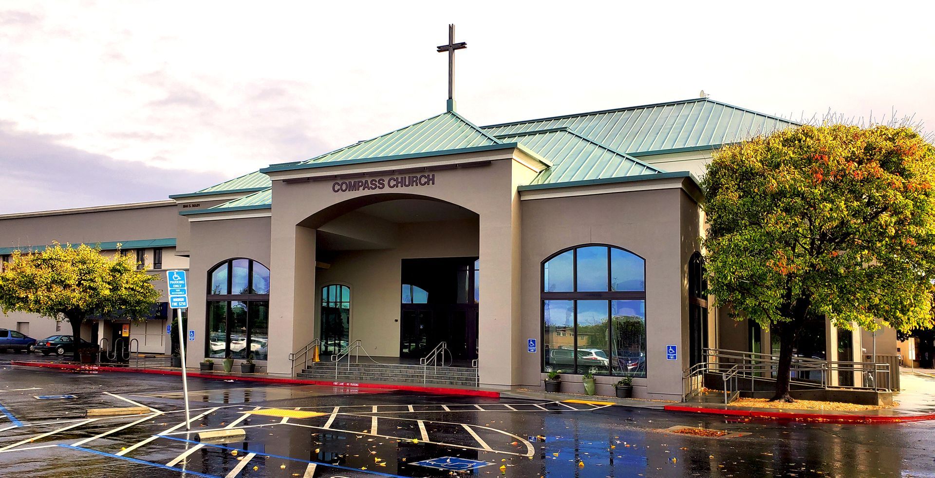 Compass Church building with a cross on top, people outside, and cars parked. in Salinas and Monterey County
