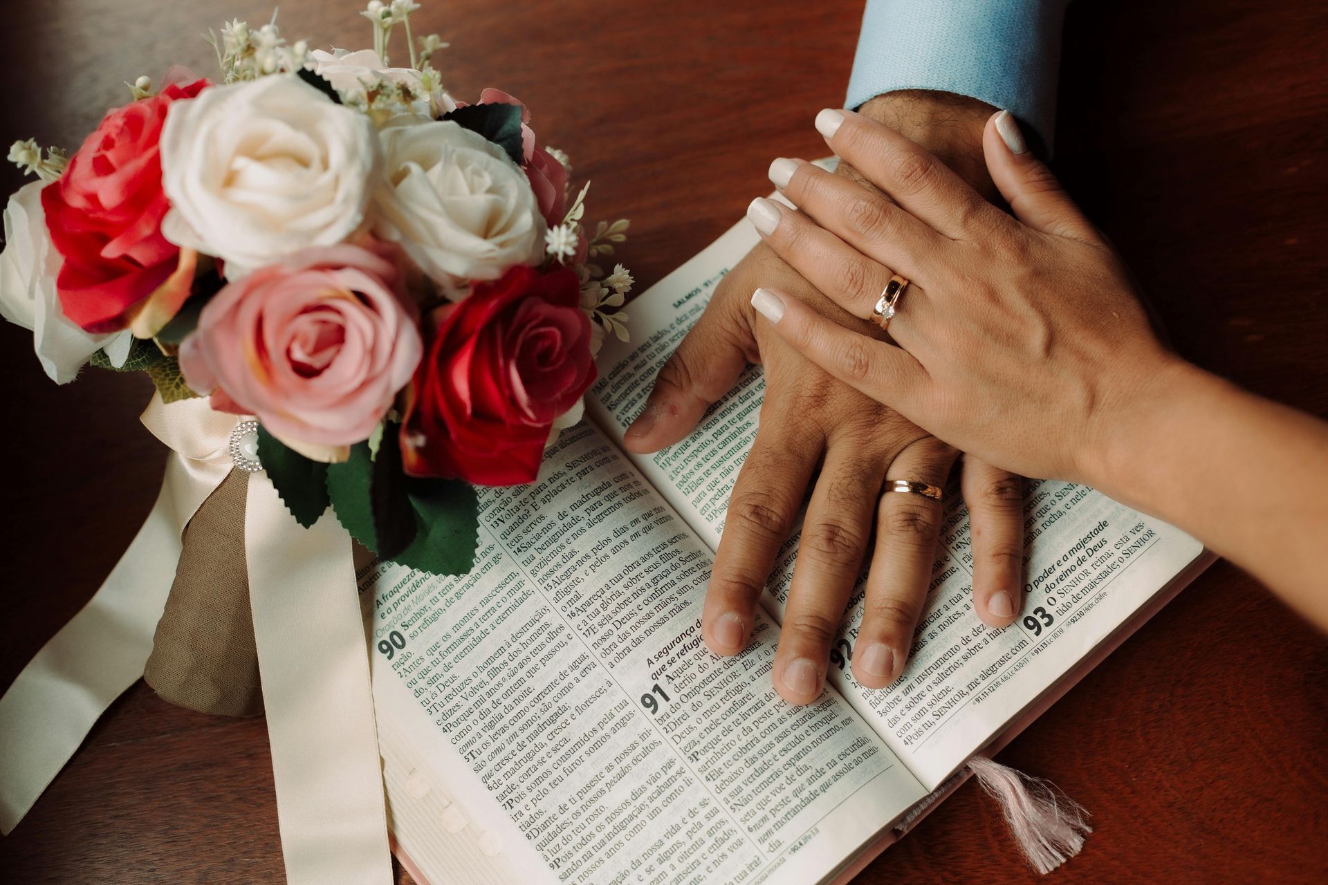 Hands with wedding rings on a book, bouquet nearby.