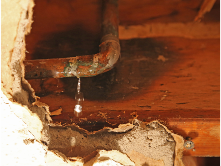 A pipe is leaking water through a hole in the wall