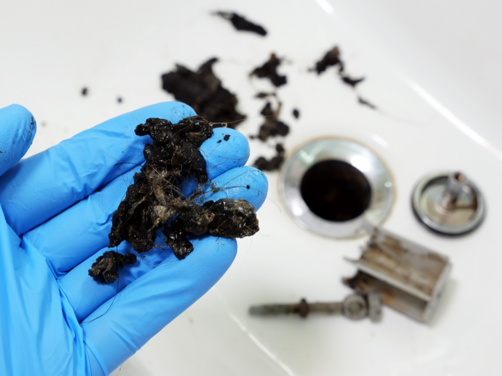 A person wearing blue gloves is holding a piece of dirt in front of a sink.