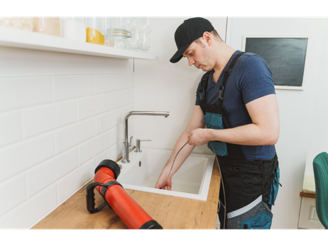 A plumber is fixing a sink in a kitchen.