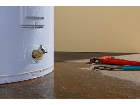 A water heater is sitting on the floor next to a pair of wrenches.