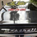 A black maserati car is parked in front of a building.