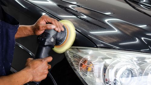 A man is polishing the hood of a car with a polisher.