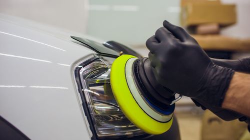 A person is polishing a car headlight with a yellow polisher.