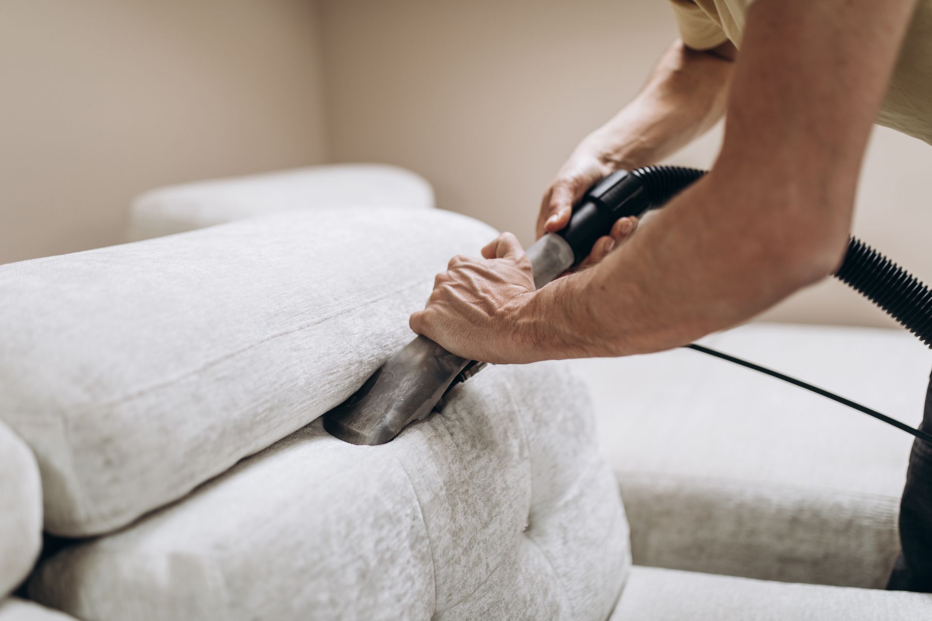 Man Cleaning a White Couch With Vacuum Cleaner