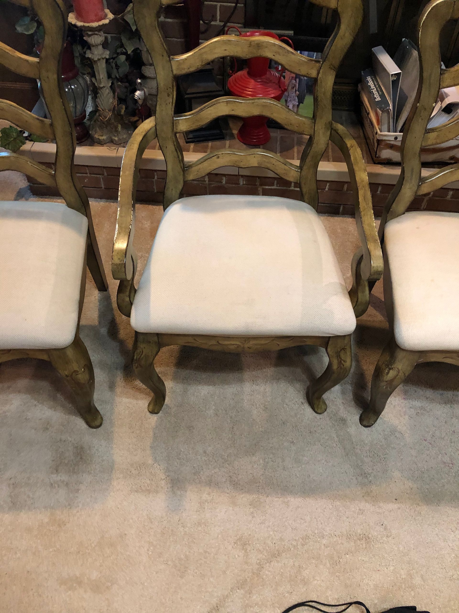 Three gold-painted chairs with white seats in a room.