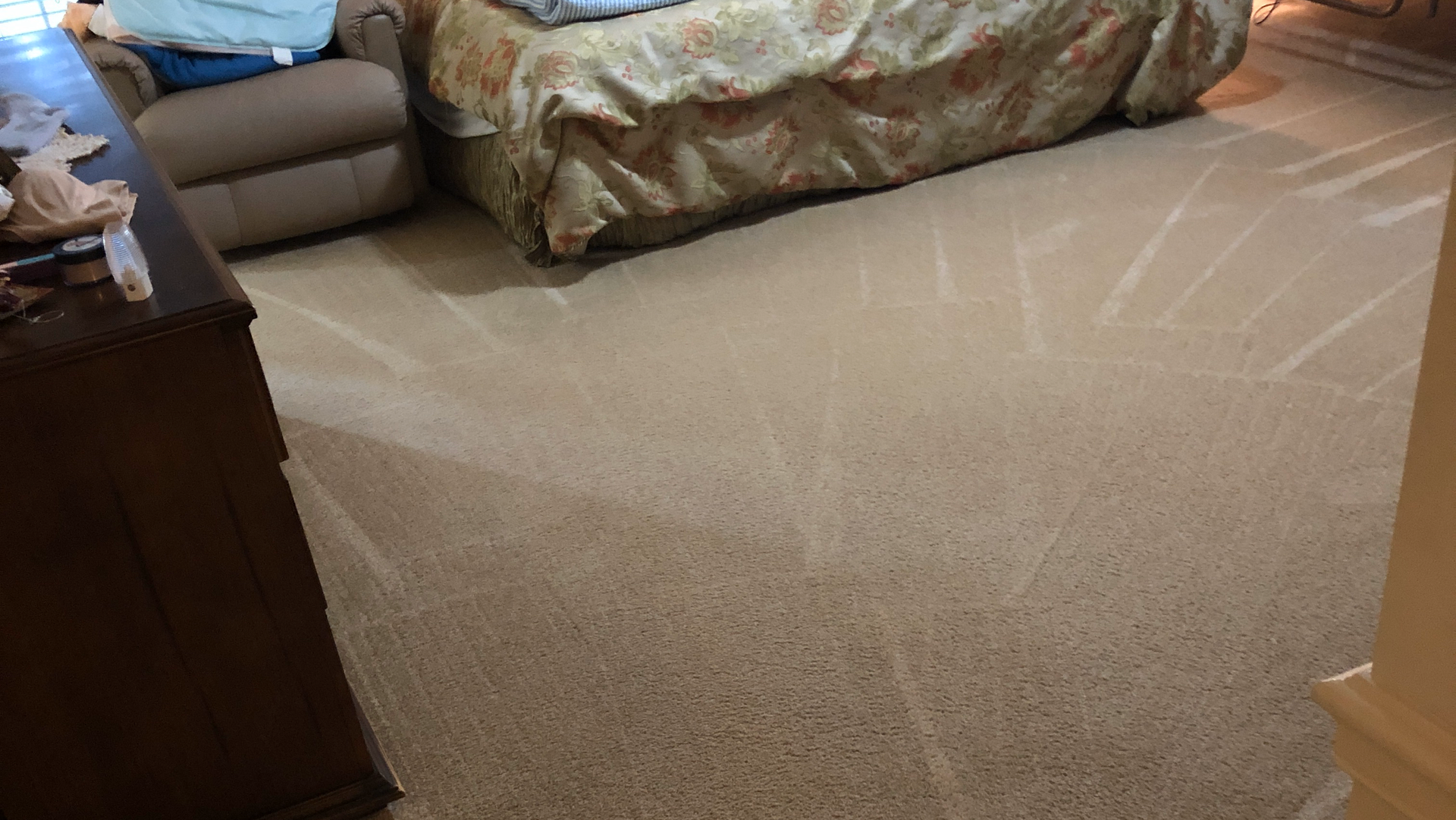 Beige carpeted bedroom with a bed, dresser, and recliner; visible cleaning marks on the floor.