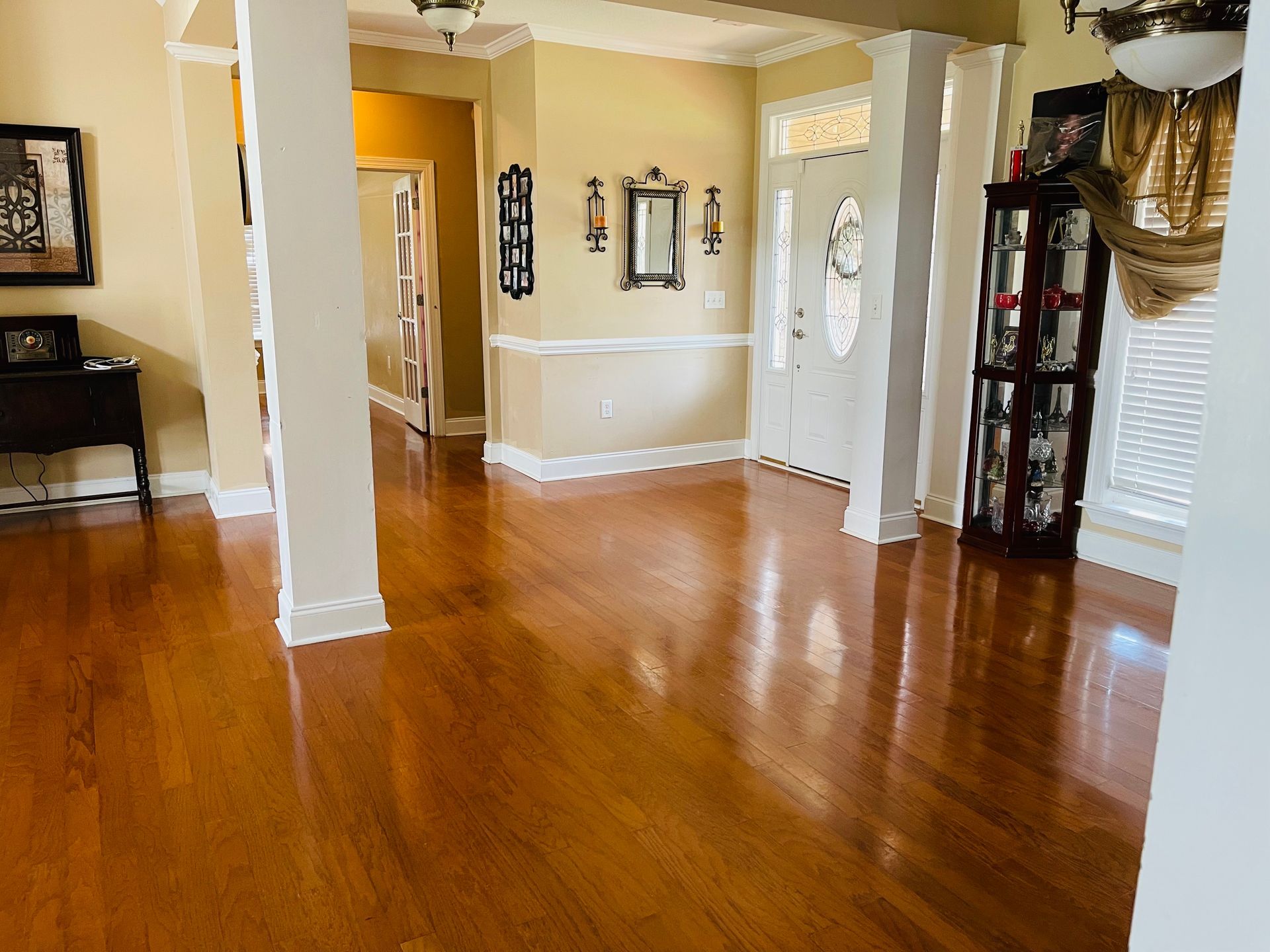 A polished hardwood floor in a well-lit entryway, with columns, and a glass-doored display cabinet.
