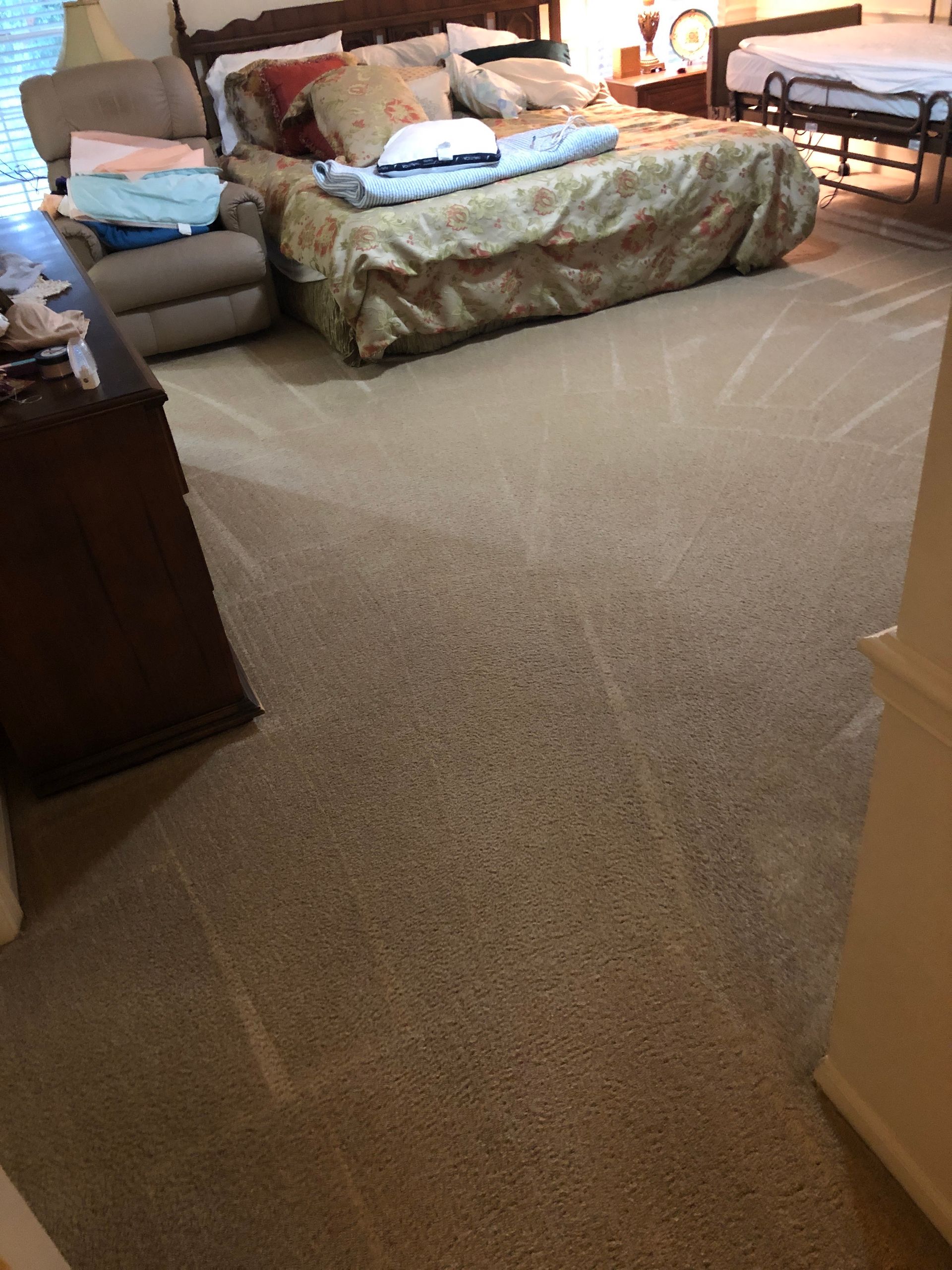 Beige carpeted bedroom with a large bed, a recliner, and a dark wooden dresser.