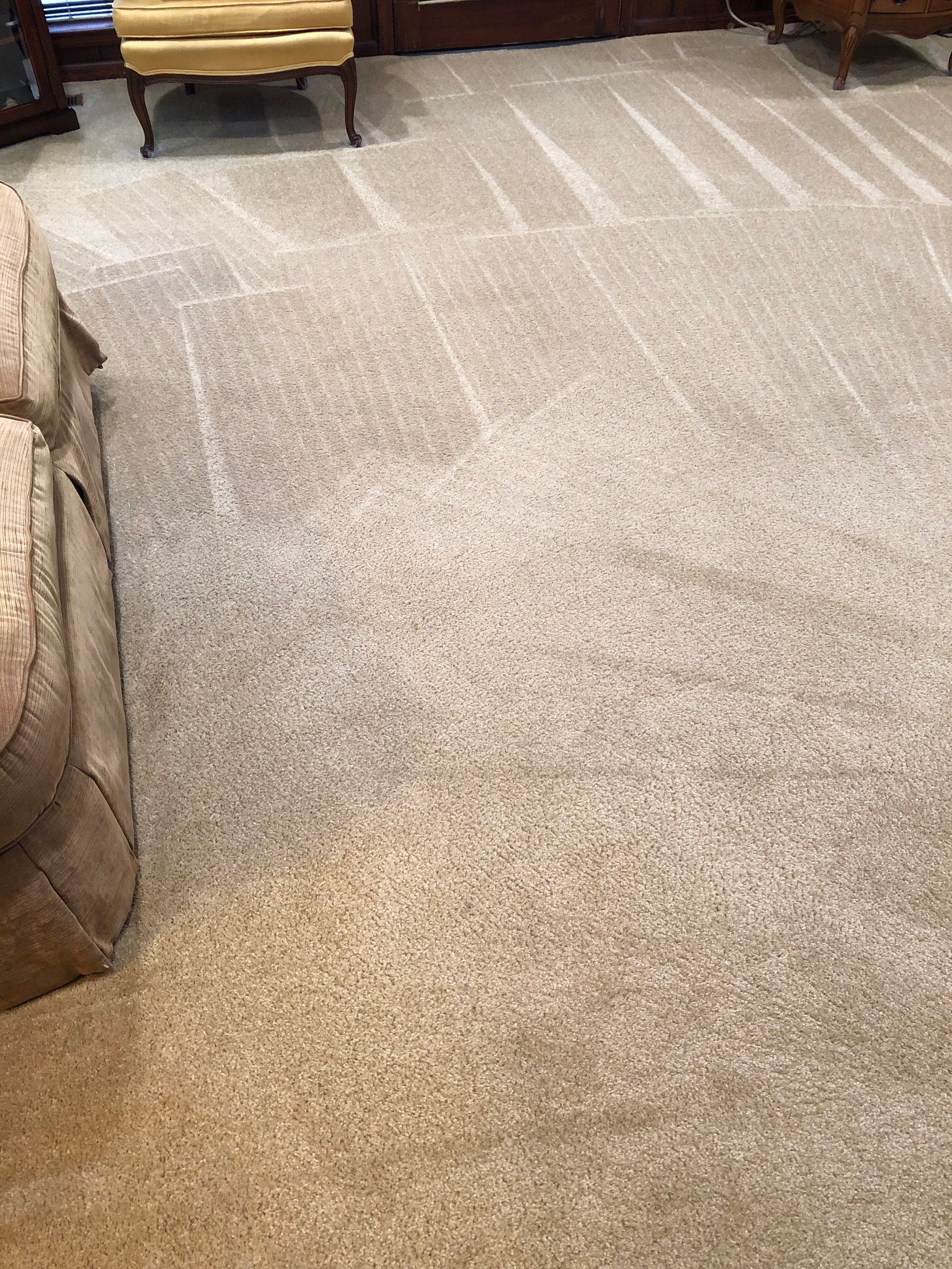 Beige carpet with faded patterns and marks, partially covered by a light brown sofa.