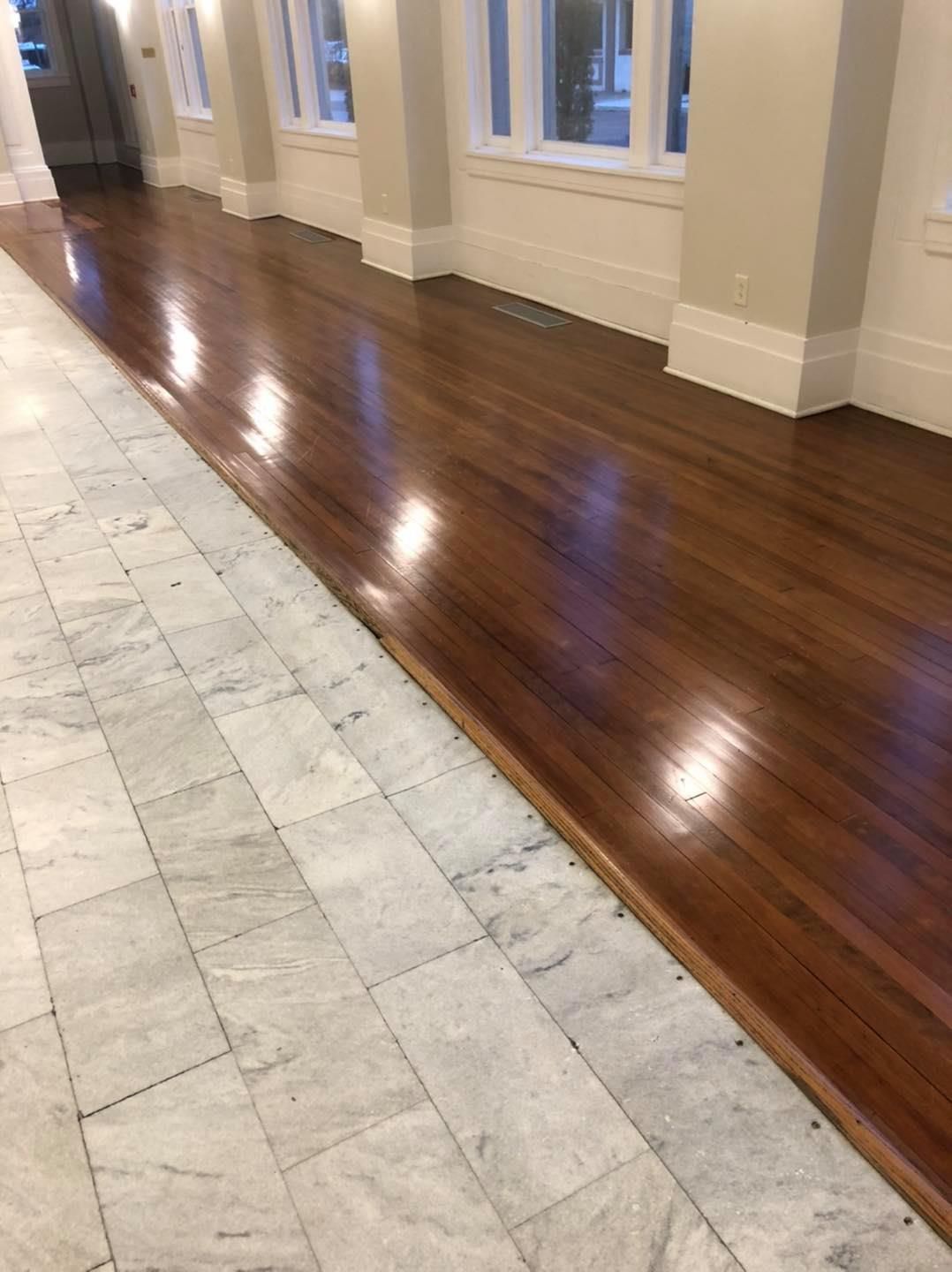 A hallway with marble flooring on the left and polished wood flooring on the right, with white pillars and windows.