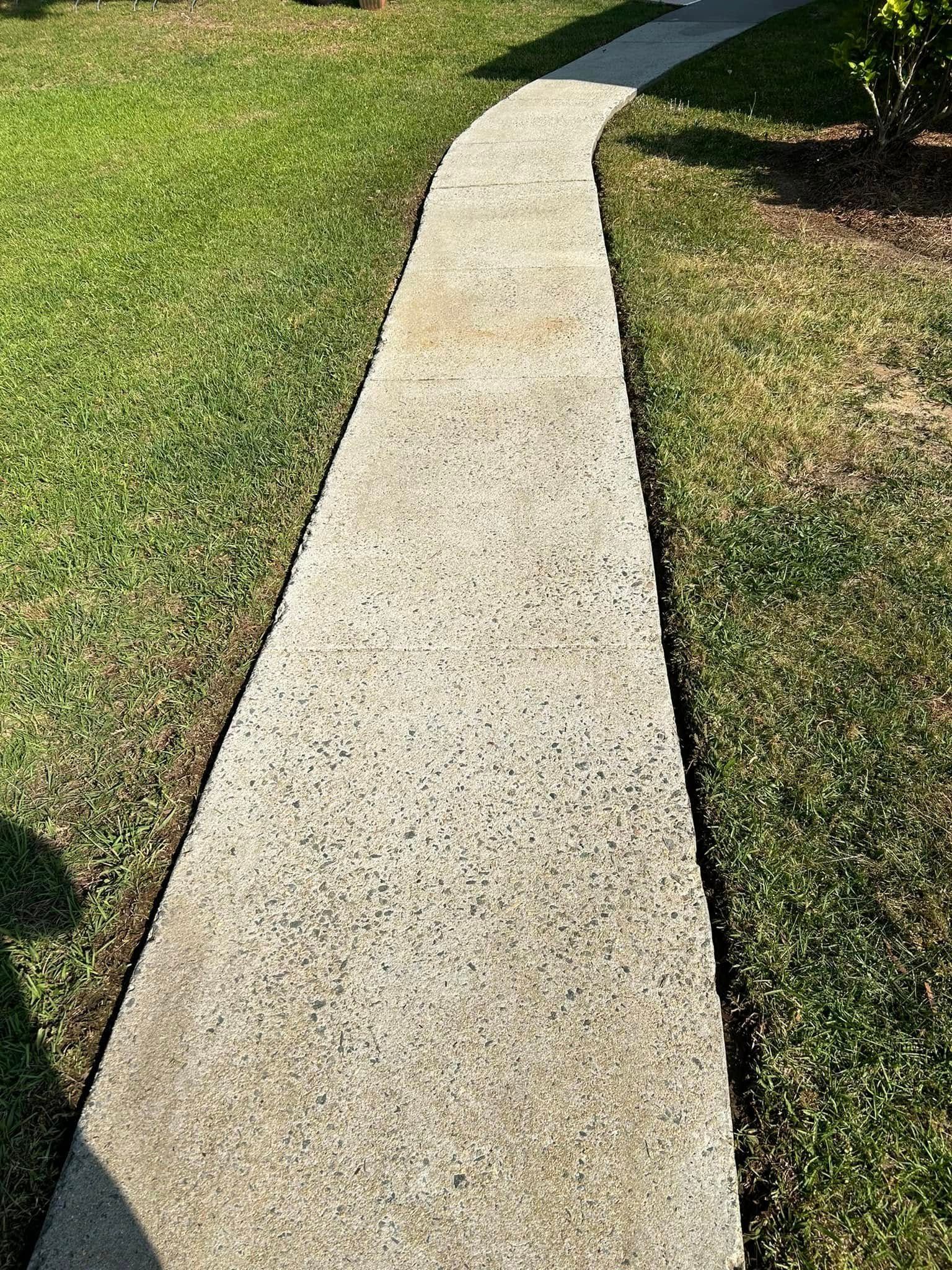 A narrow concrete walkway curves through green grass in an outdoor setting.
