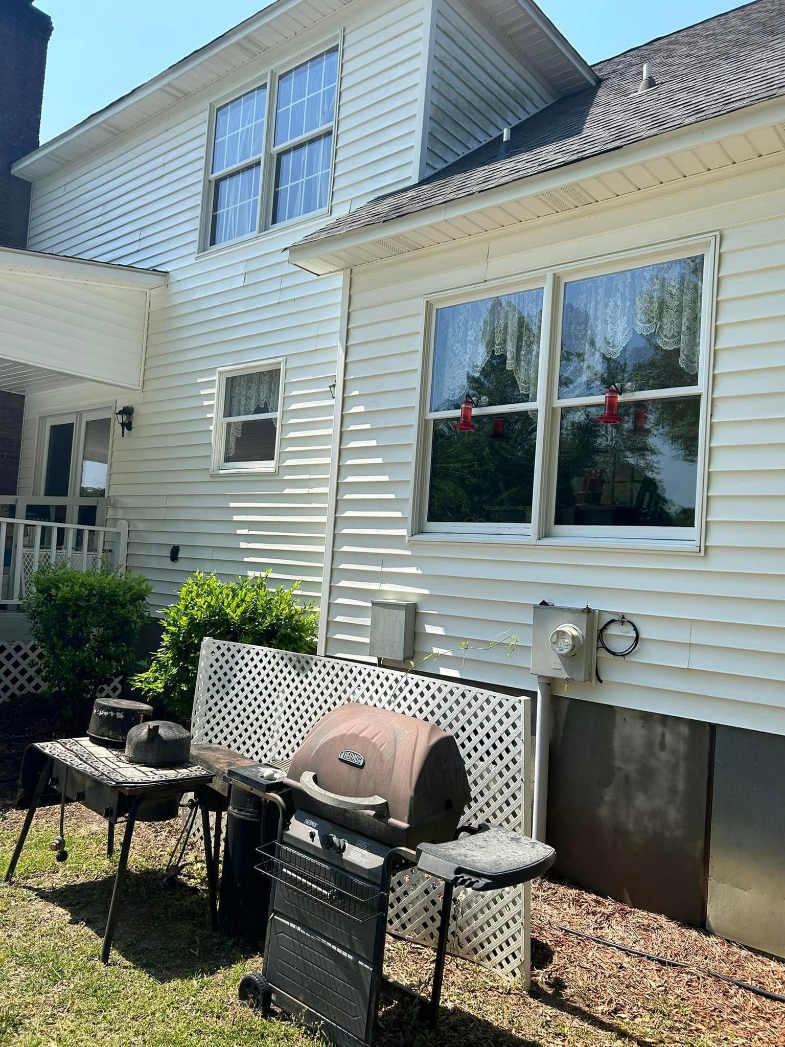 White house exterior with a grill, outdoor seating, and windows on a sunny day.
