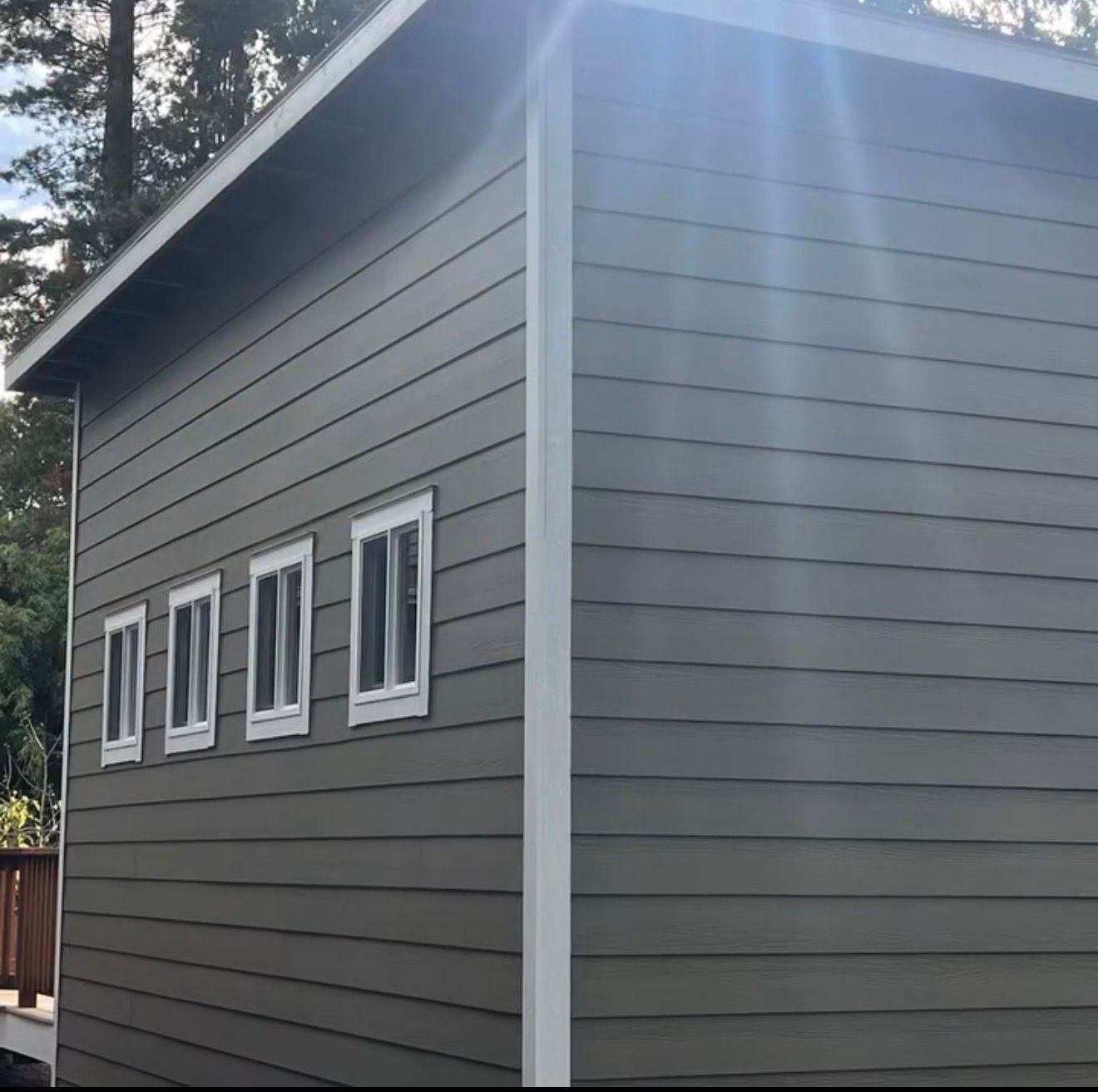 Covered wooden deck with steps leading up to a house. Exterior shot with siding and a glimpse of trees.