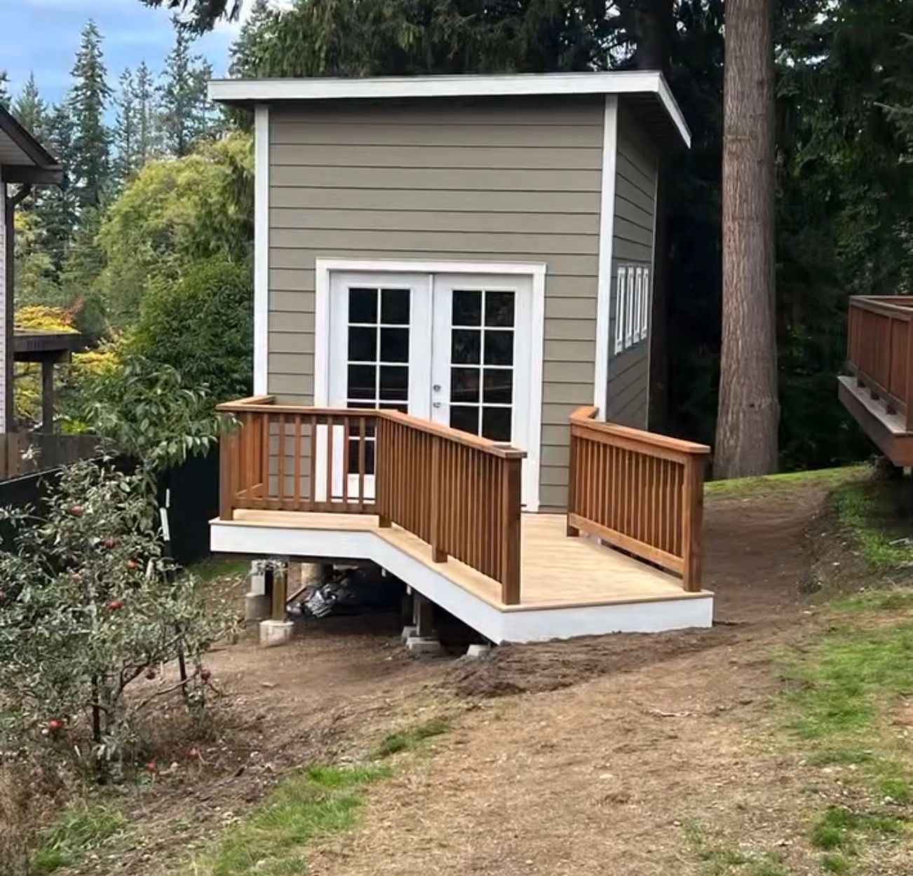 Wooden deck with ramp and handrail leading to white French doors on a building with green siding.