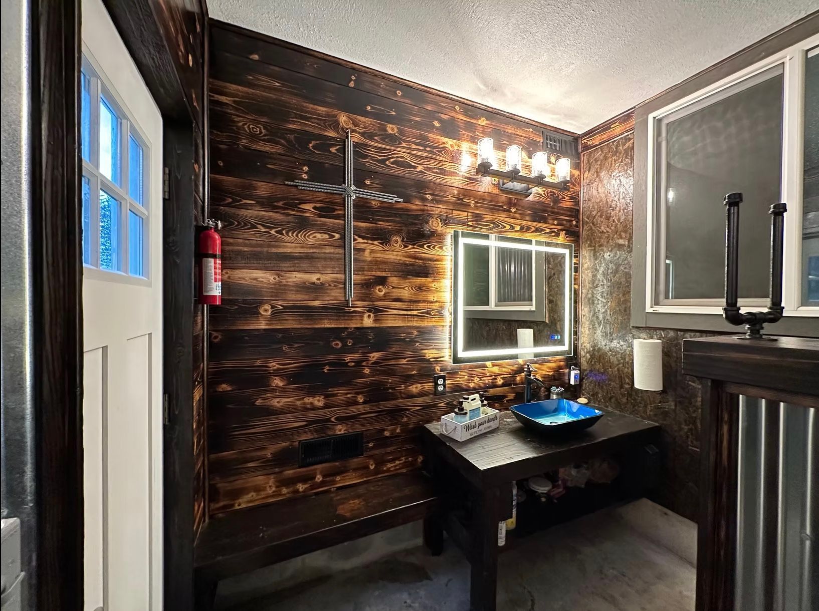 Rustic bathroom with charred wood walls, blue glass sink, and industrial accents.
