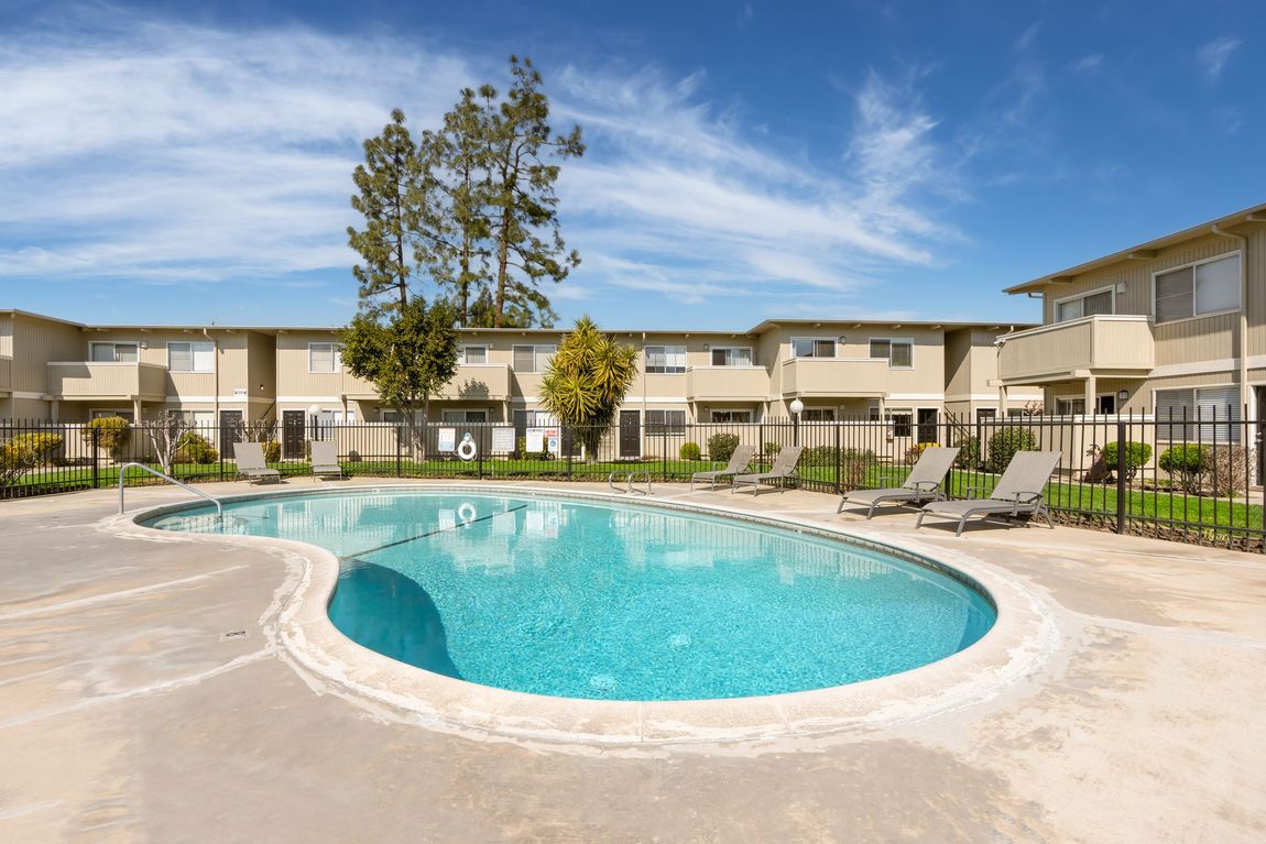 A swimming pool in front of apartment buildings on a sunny day.