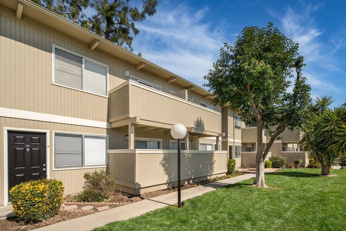 Apartment building exterior with tan siding, balconies, and a green lawn under a blue sky.