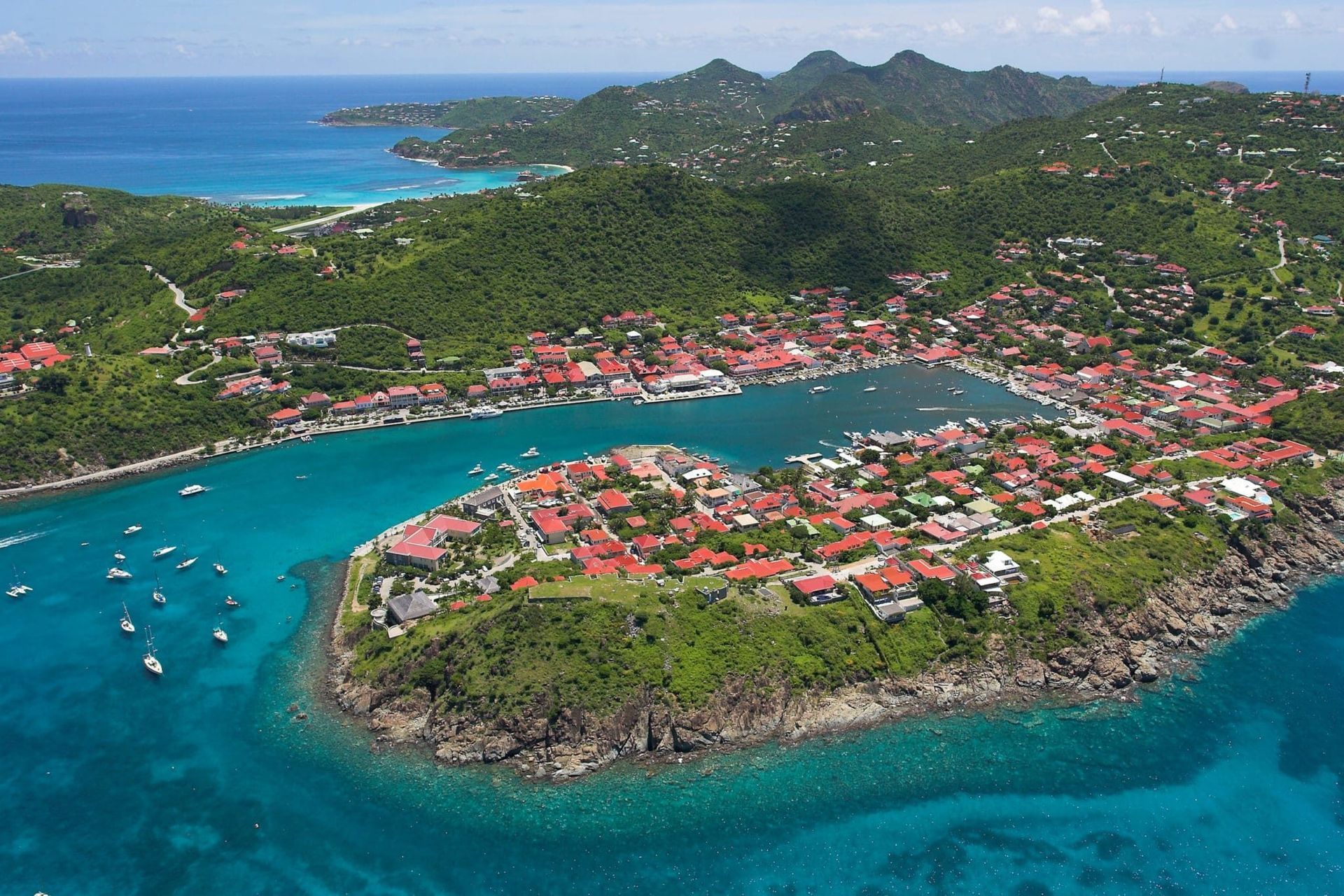 Aerial view of a coastal town on a Caribbean island, with turquoise water and green hills.
