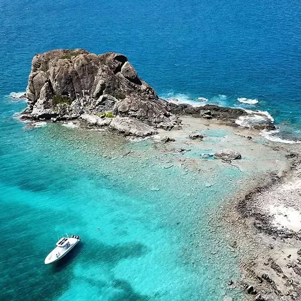 Rocky islet in turquoise water with a boat nearby.