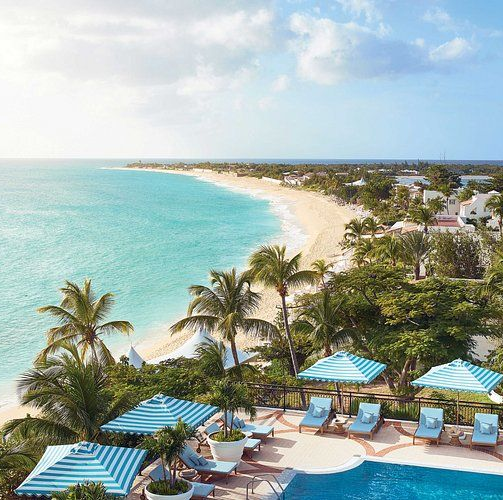 Beach resort with pool and umbrellas overlooking turquoise water and white sand beach.