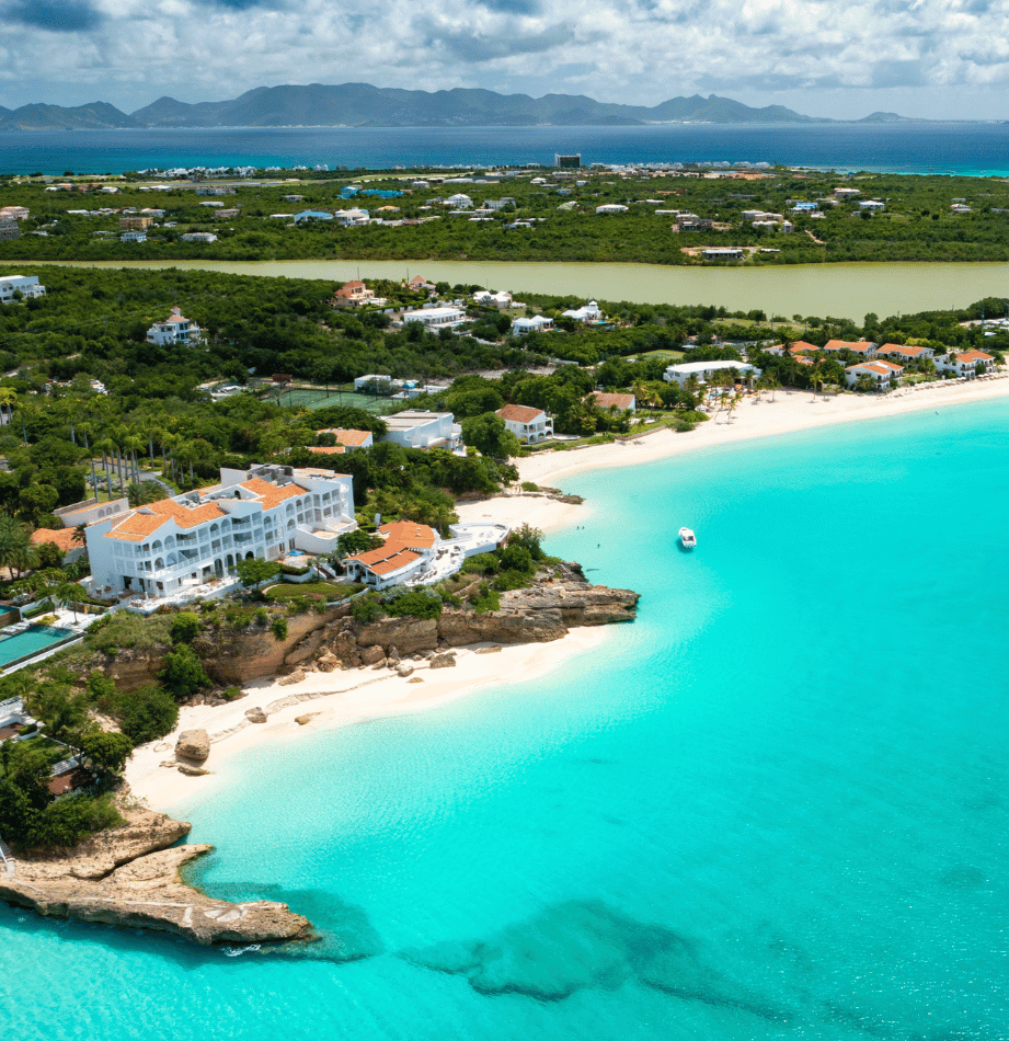 Turquoise water laps a white sandy beach with a resort, lush greenery, and distant mountains.