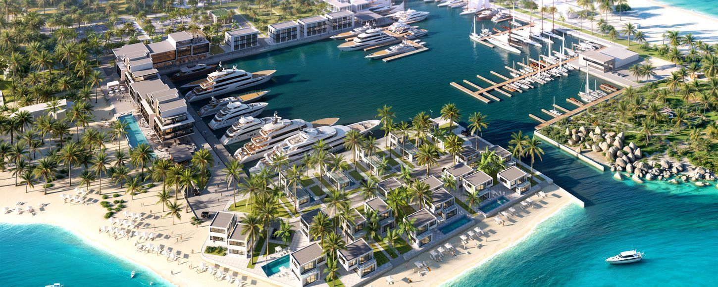 Aerial view of a coastal marina with boats, buildings, beach, and blue water.