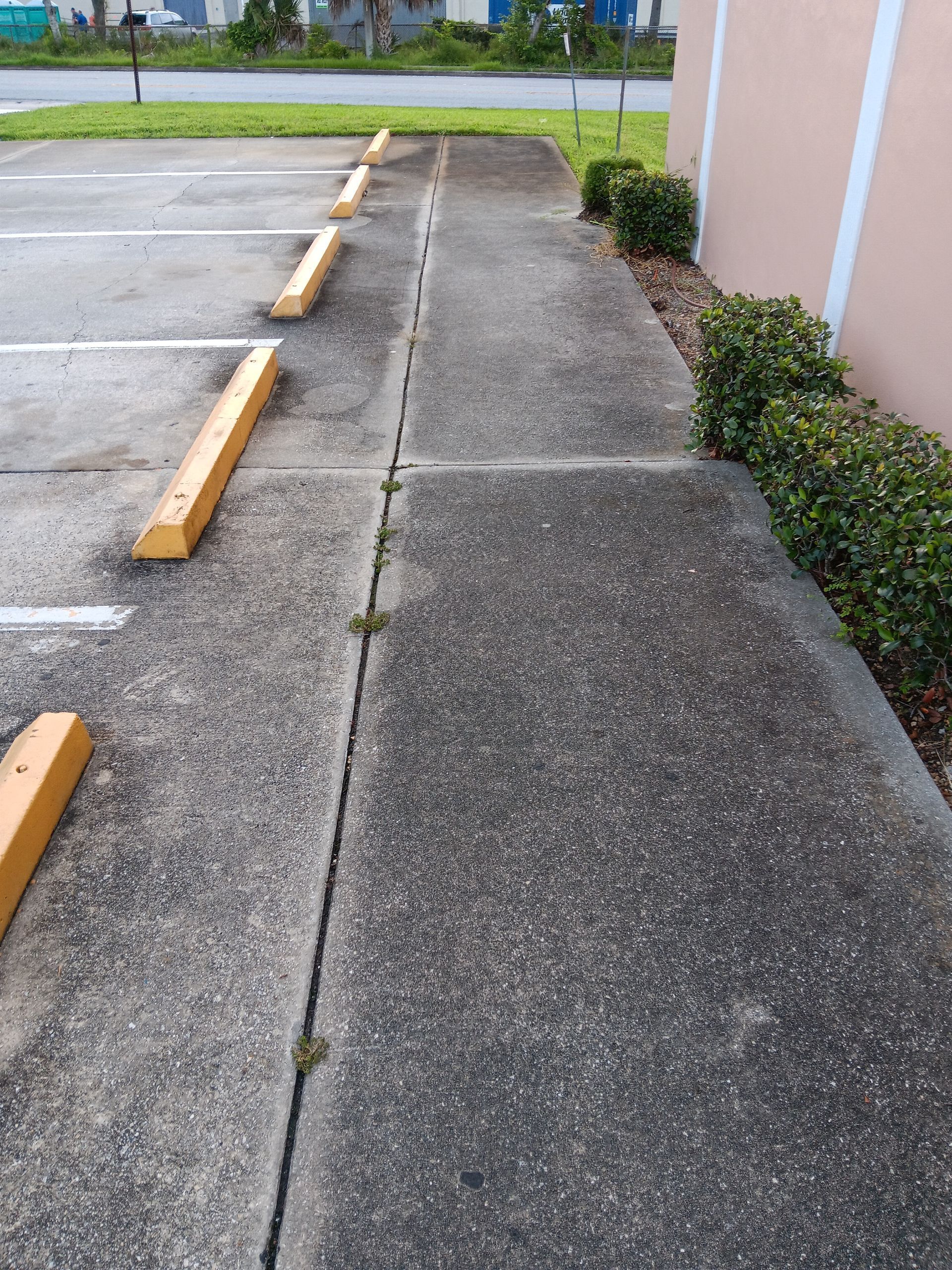A sidewalk leading to a parking lot with yellow parking blocks