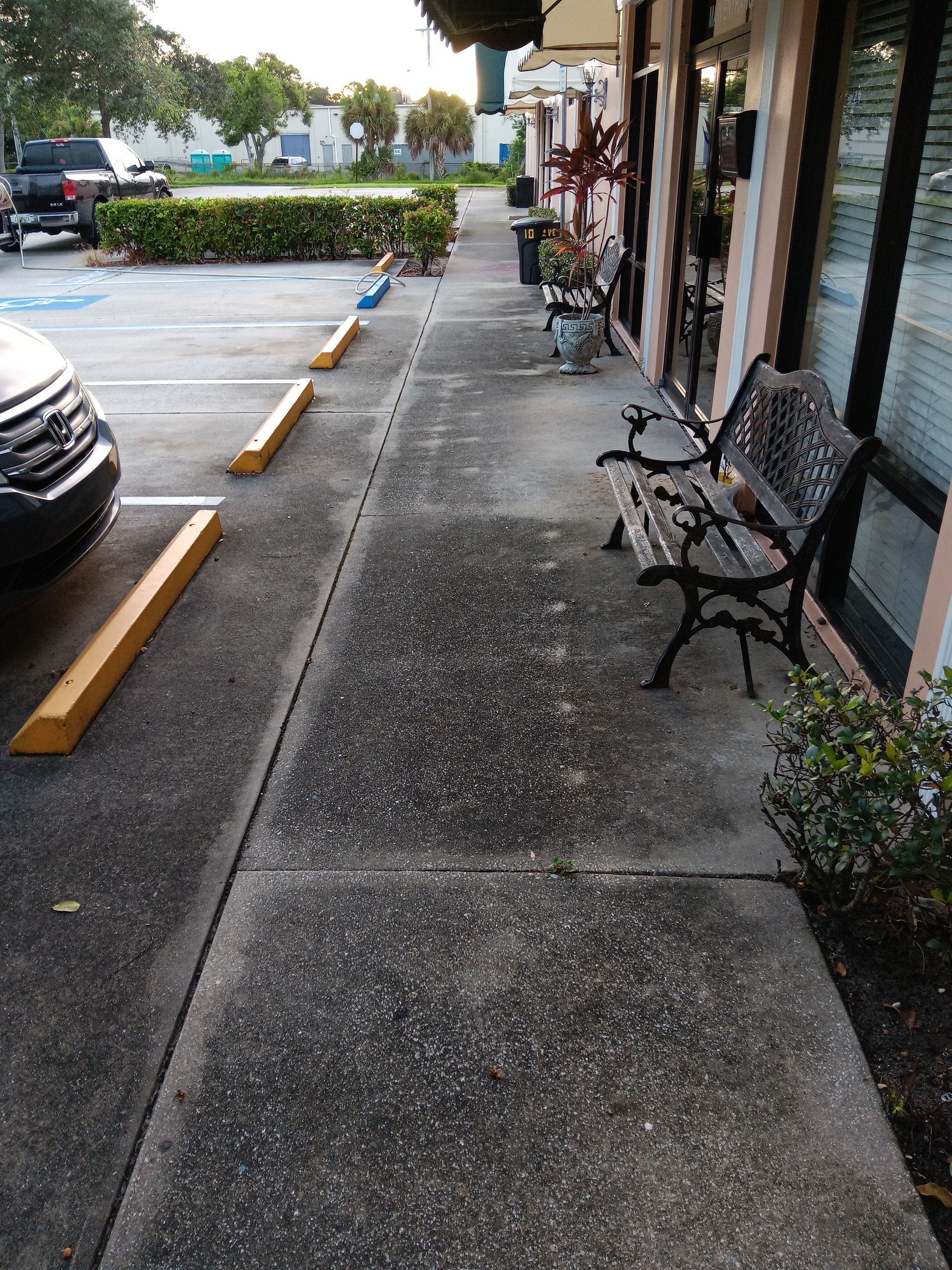 A sidewalk with a bench and a parking lot in the background