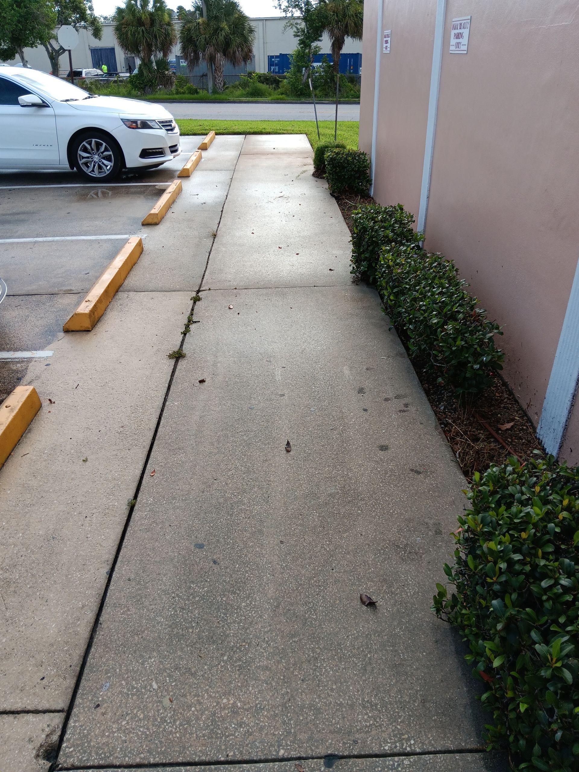 A white car is parked in a parking lot next to a sidewalk