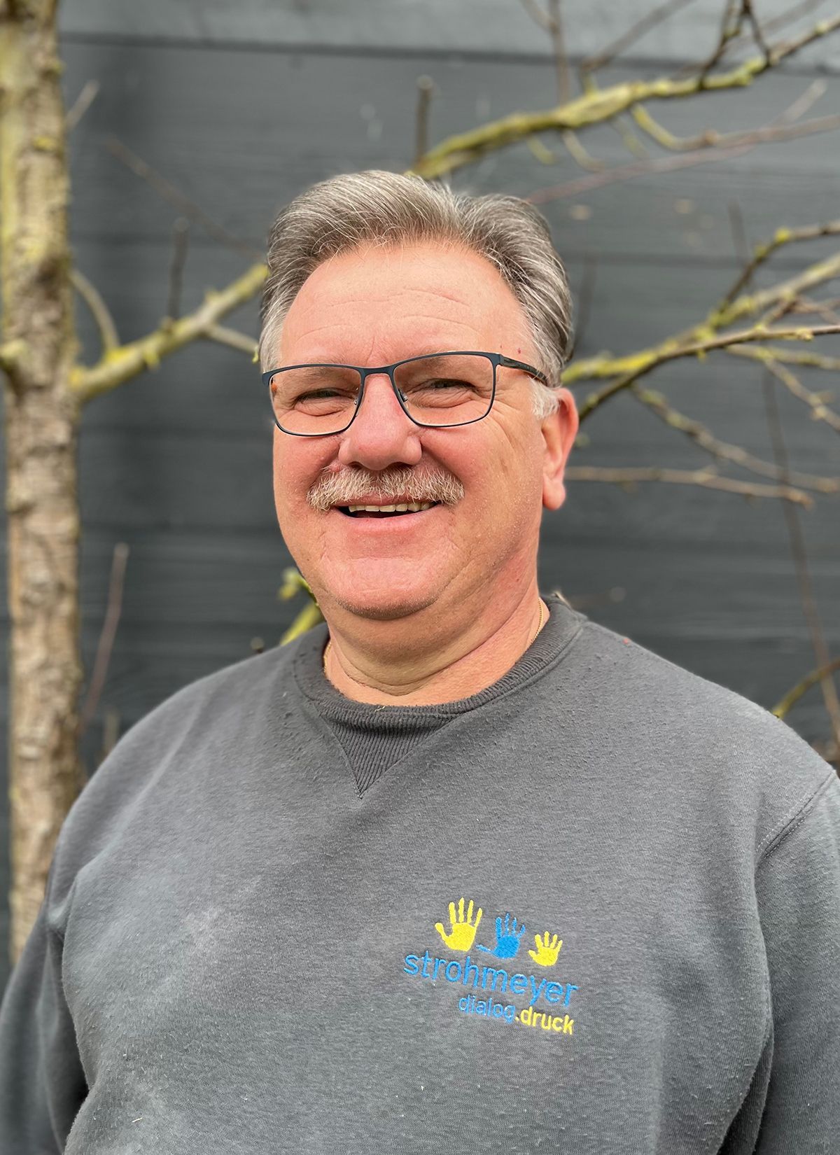 Ein Mann mit Brille und Schnurrbart lächelt in die Kamera.