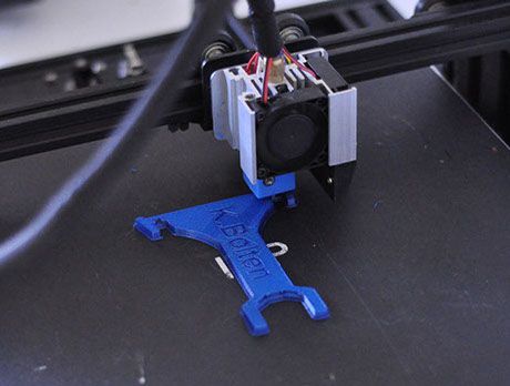 Ein 3D-Drucker druckt ein blaues Objekt auf eine schwarze Oberfläche.