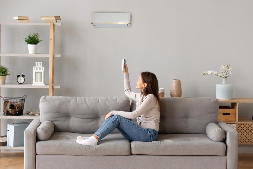 A Woman Sitting on a Couch Holding a Remote Control for an Air Conditioner — Refrigerated Technologies (QLD) Pty Ltd In Cannonvale, QLD