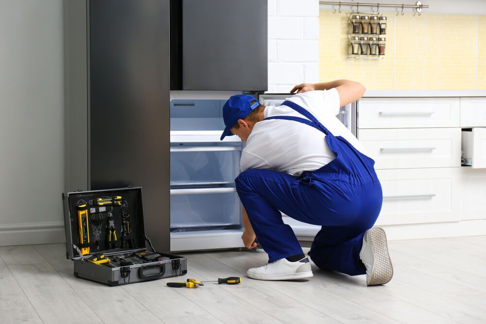 A Man Repairs a Refrigerator in a Kitchen — Refrigerated Technologies (QLD) Pty Ltd In Airlie Beach, QLD