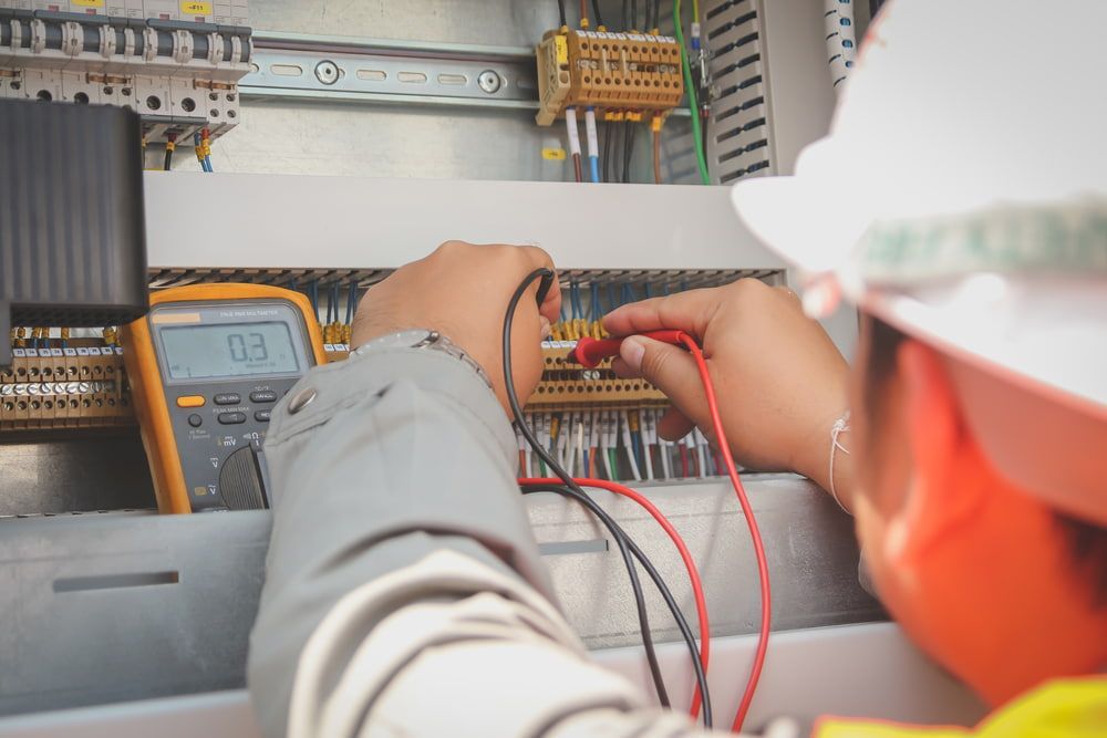 A Man is Working on an Electrical Box With a Multimeter — Refrigerated Technologies (QLD) Pty Ltd In Airlie Beach, QLD