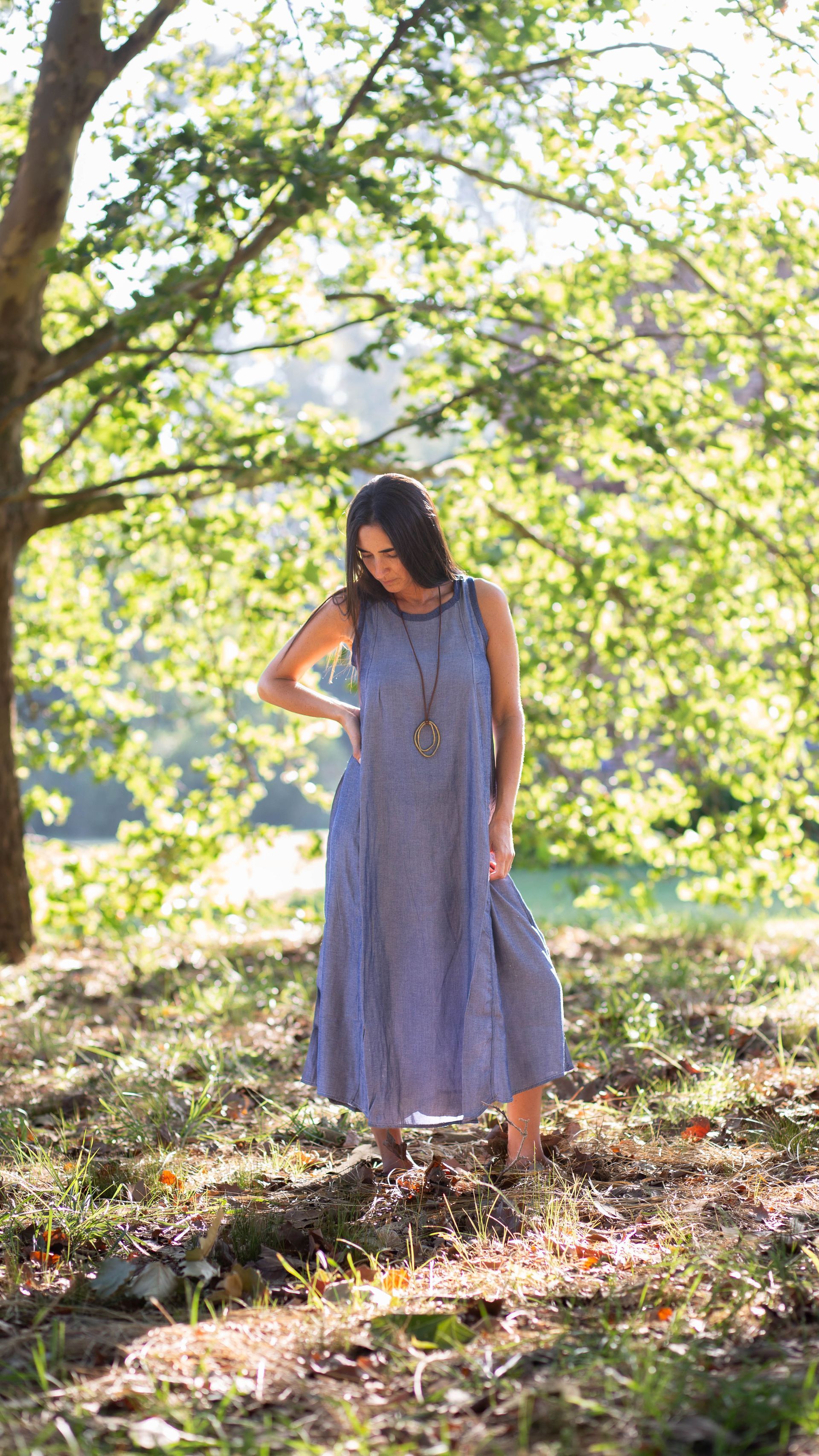 Dos mujeres, al aire libre, sonriendo; una con un vestido de rayas, otra con un vestido azul, de pie cerca de un árbol.