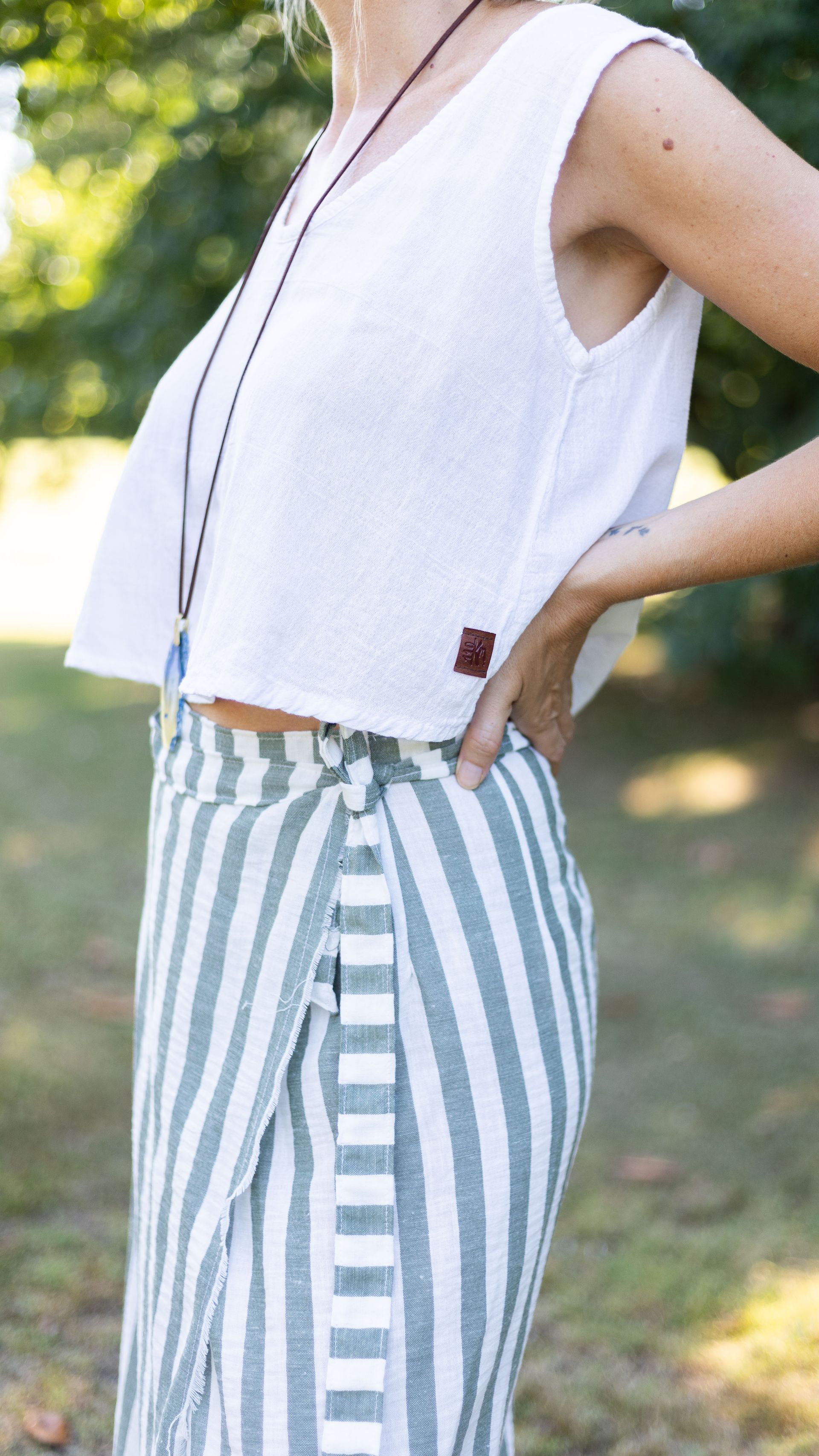 Mujer con top corto blanco y falda cruzada de rayas verdes, mano en la cadera al aire libre.