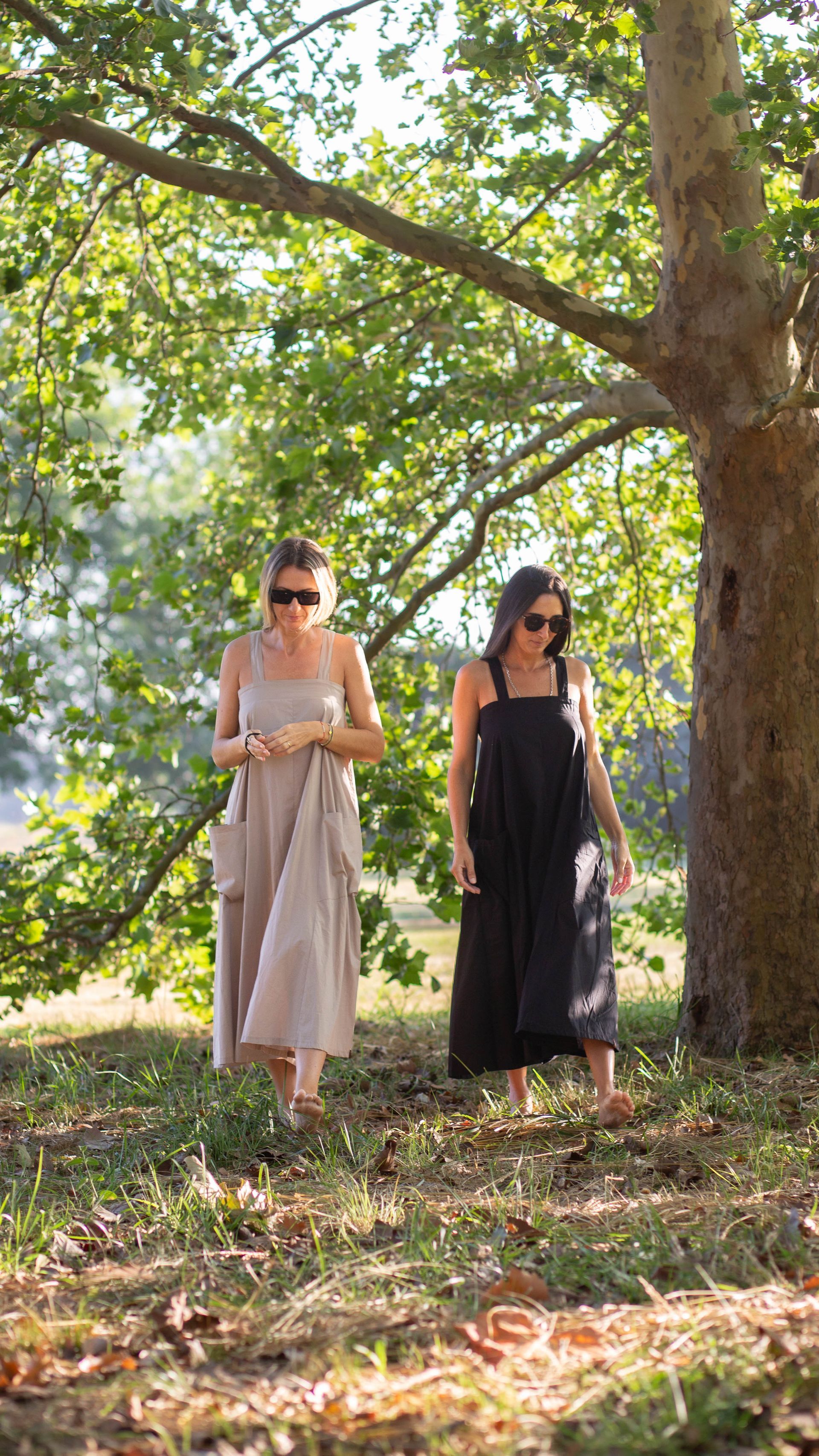 Mujer con un vestido rosa de pie descalza en un parque soleado, con la mano en el cabello.