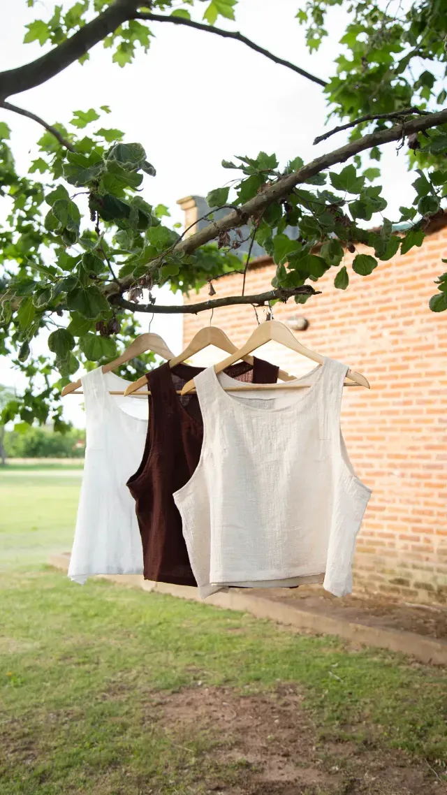 Mujer vestida de lino marrón con collar colgante, de pie sobre el césped.