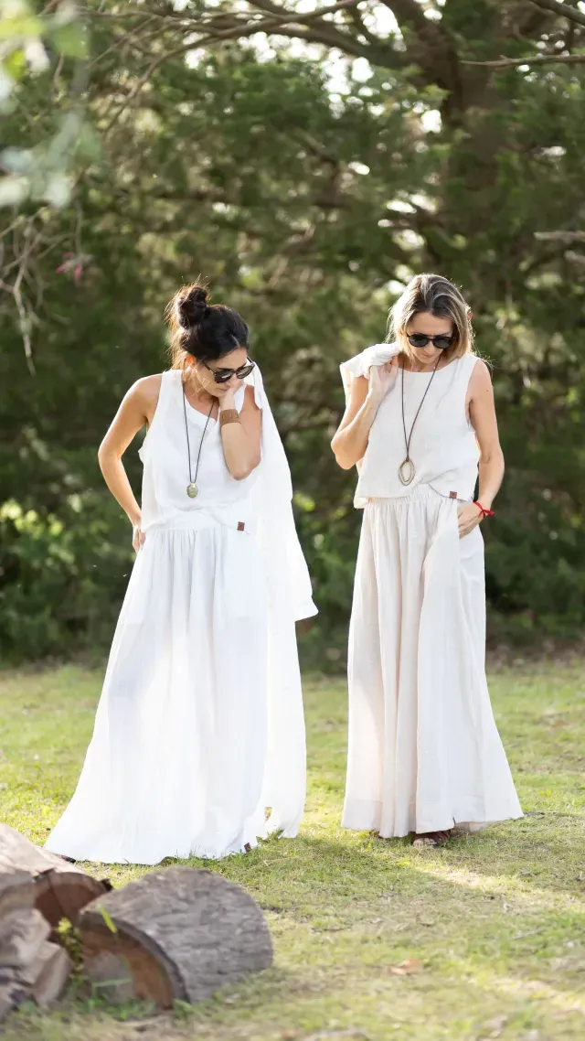 Dos mujeres vestidas de blanco y con gafas de sol, posando al aire libre.