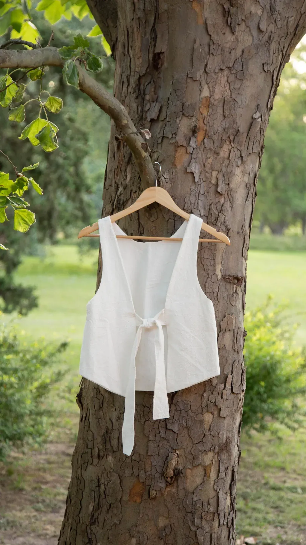 Cuatro chalecos de color marrón, crema, tostado y azul cuelgan de la rama de un árbol al aire libre.