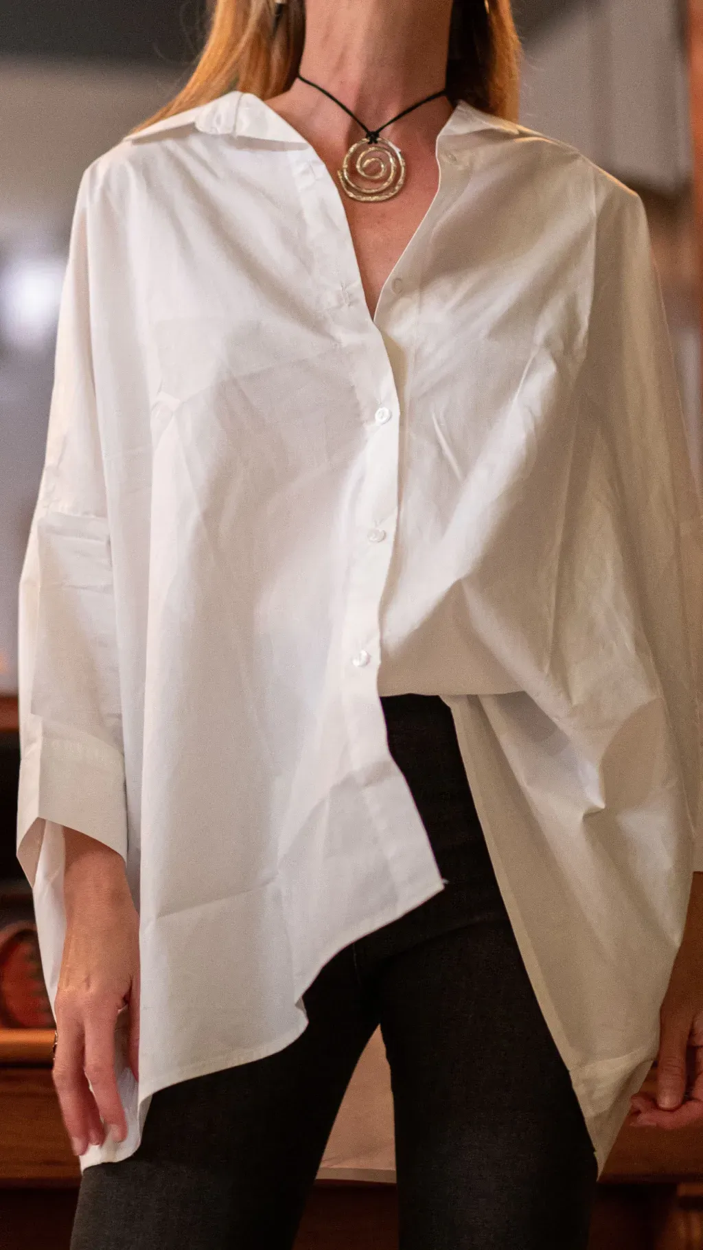 Mujer vestida con una camisa blanca de gran tamaño y pantalones oscuros, con un collar.