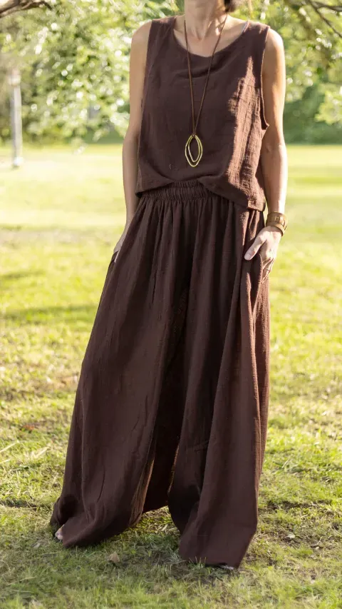 Mujer vestida de lino marrón con collar colgante, de pie sobre el césped.