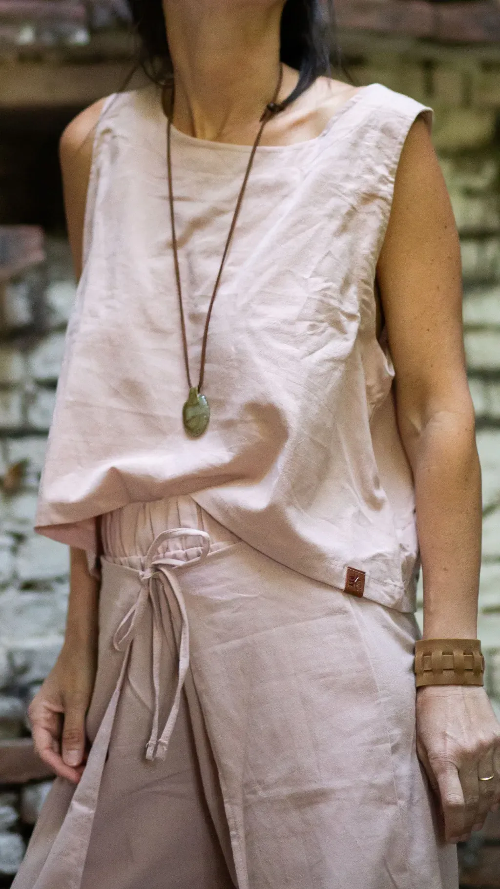 Mujer con una camiseta sin mangas de color rosa claro y pantalones a juego, luciendo un collar y una pulsera.